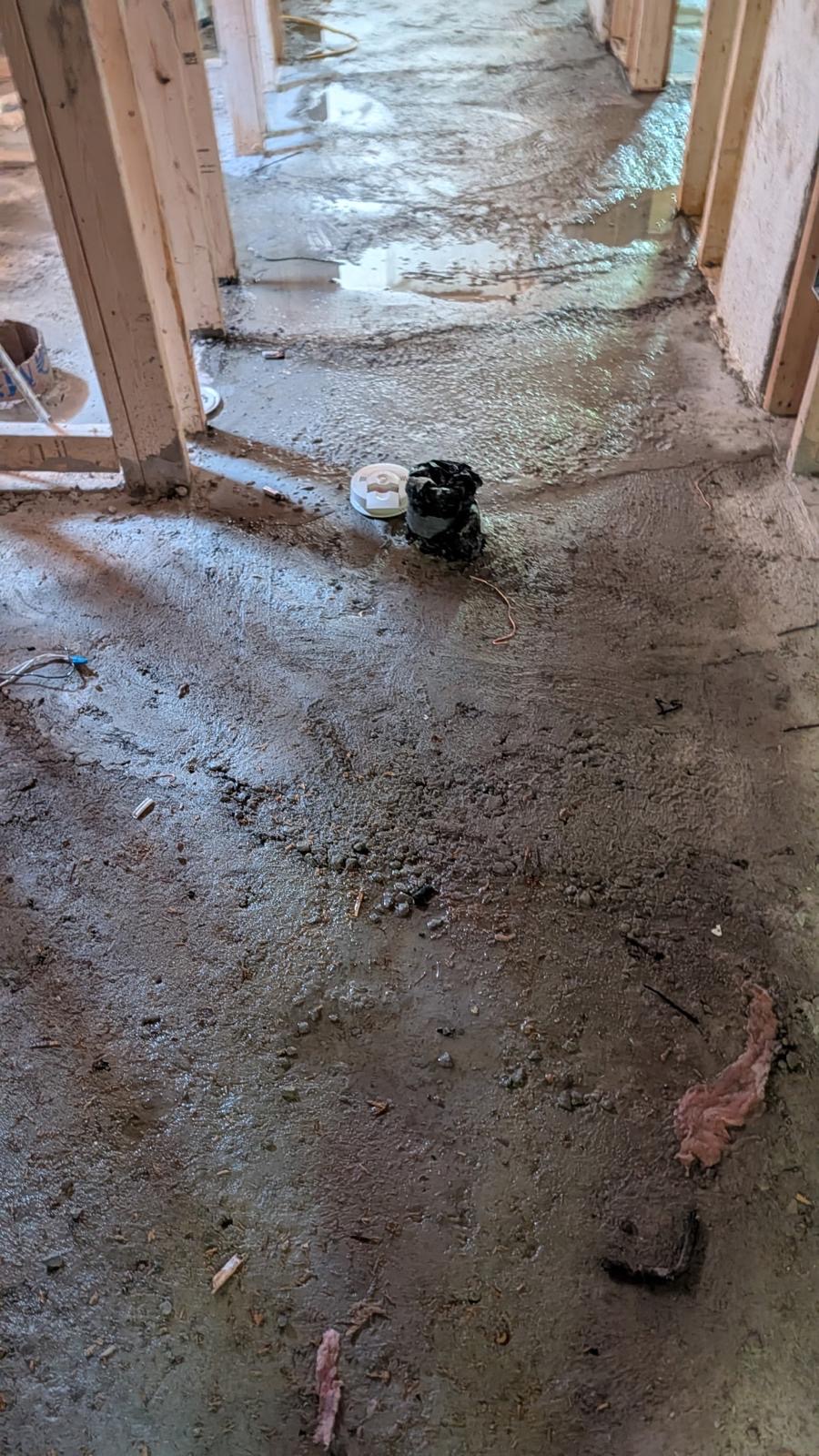 Rough uneven concrete basement subfloor between wood framing before floor levelling