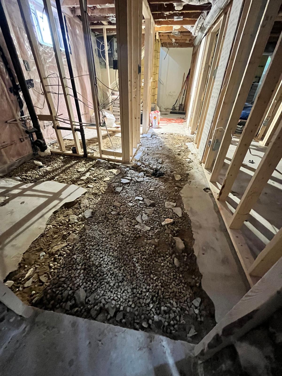 Gravel and rubble subfloor between basement framing before concrete floor levelling