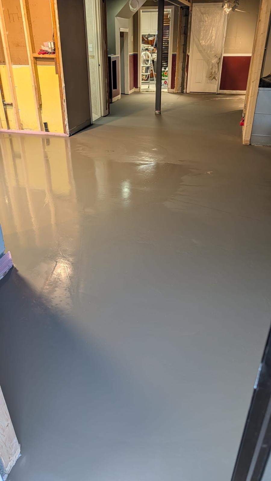 Freshly poured grey self-levelling cement flowing through a home basement hallway