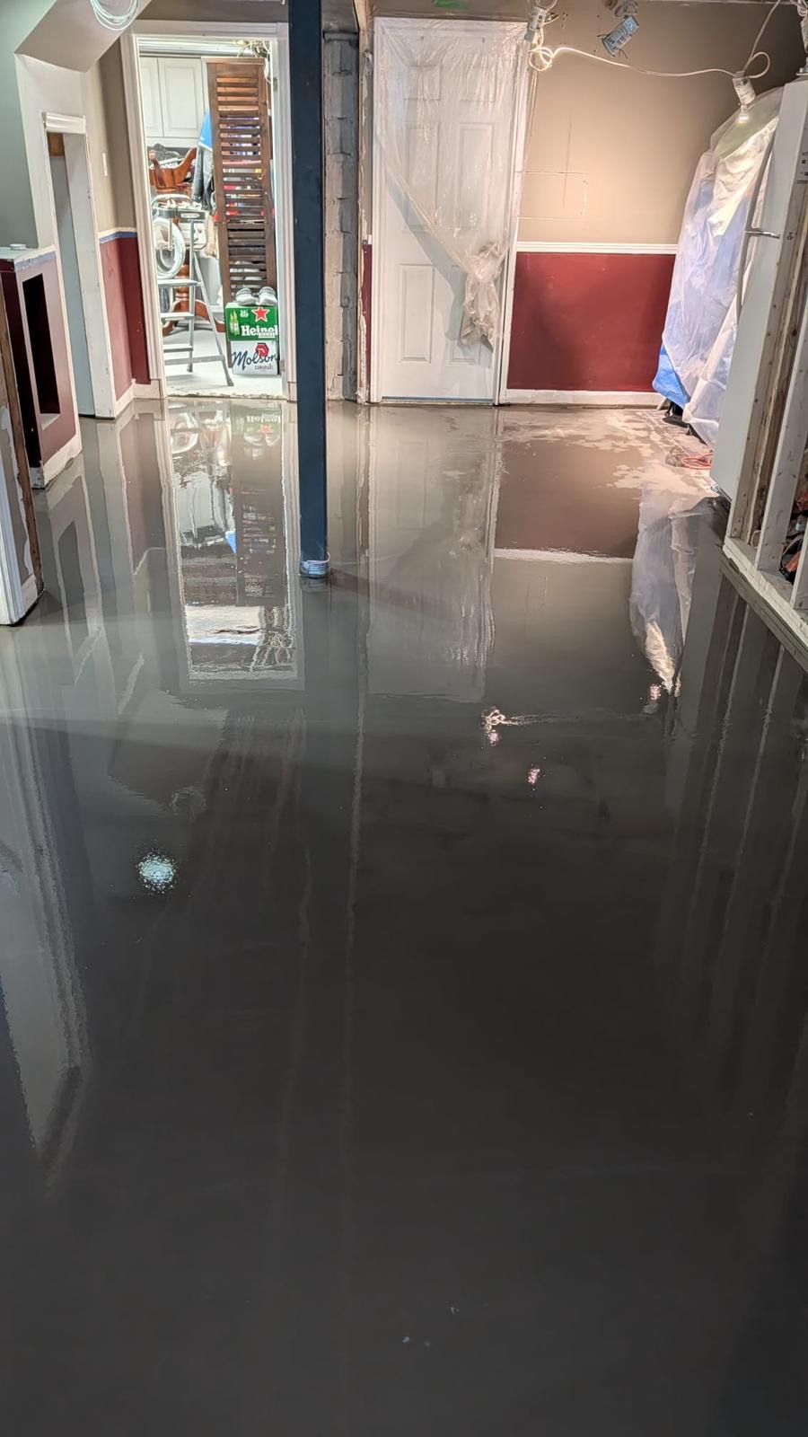 Glossy self-levelling compound covering a home basement floor with plastic-sheeted doorways