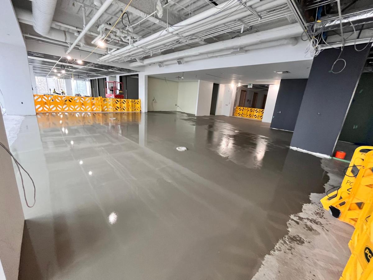 Self-levelling cement pour spreading across a Toronto office floor behind yellow barricades