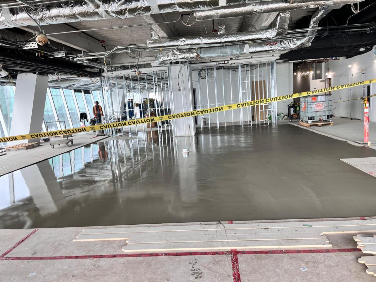 Large self-levelling underlayment pour across a Toronto office floor with caution tape and exposed ceiling