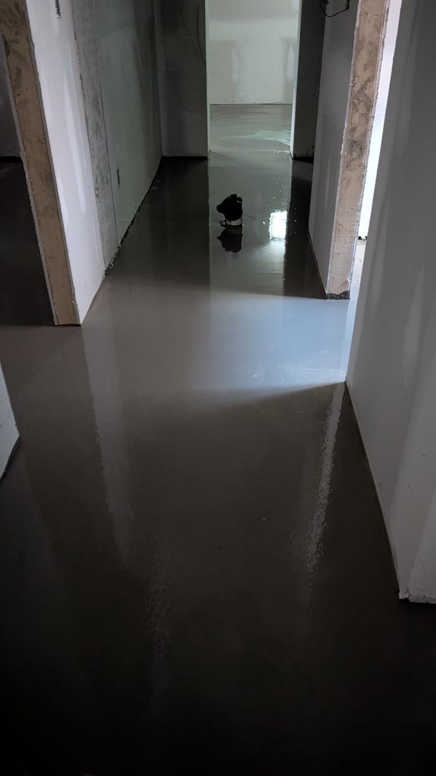Glossy self-levelling underlayment poured down a narrow hallway between white walls