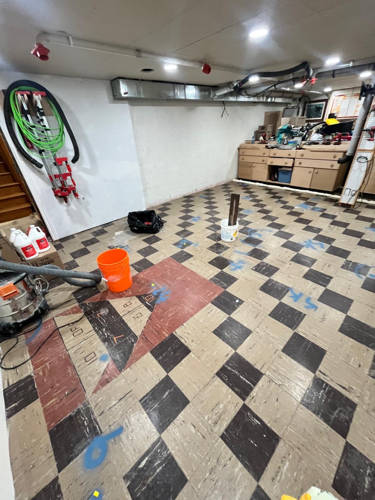 Old checkerboard vinyl tile workshop floor with tools and buckets before self-levelling