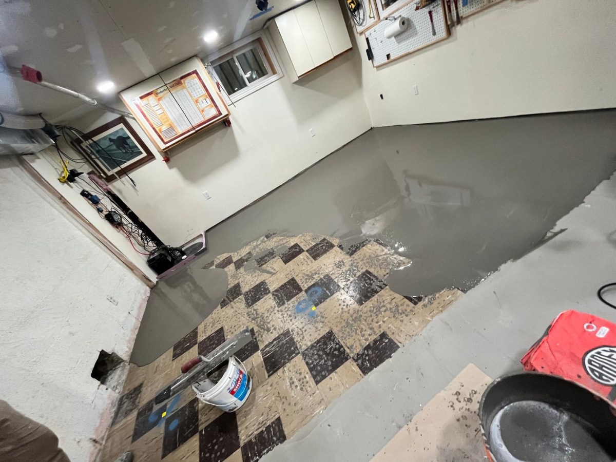 Self-levelling cement spreading over old checkerboard tile in a home workshop mid-pour